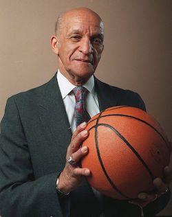 A man in a suite stands holding a basketball in his hands.