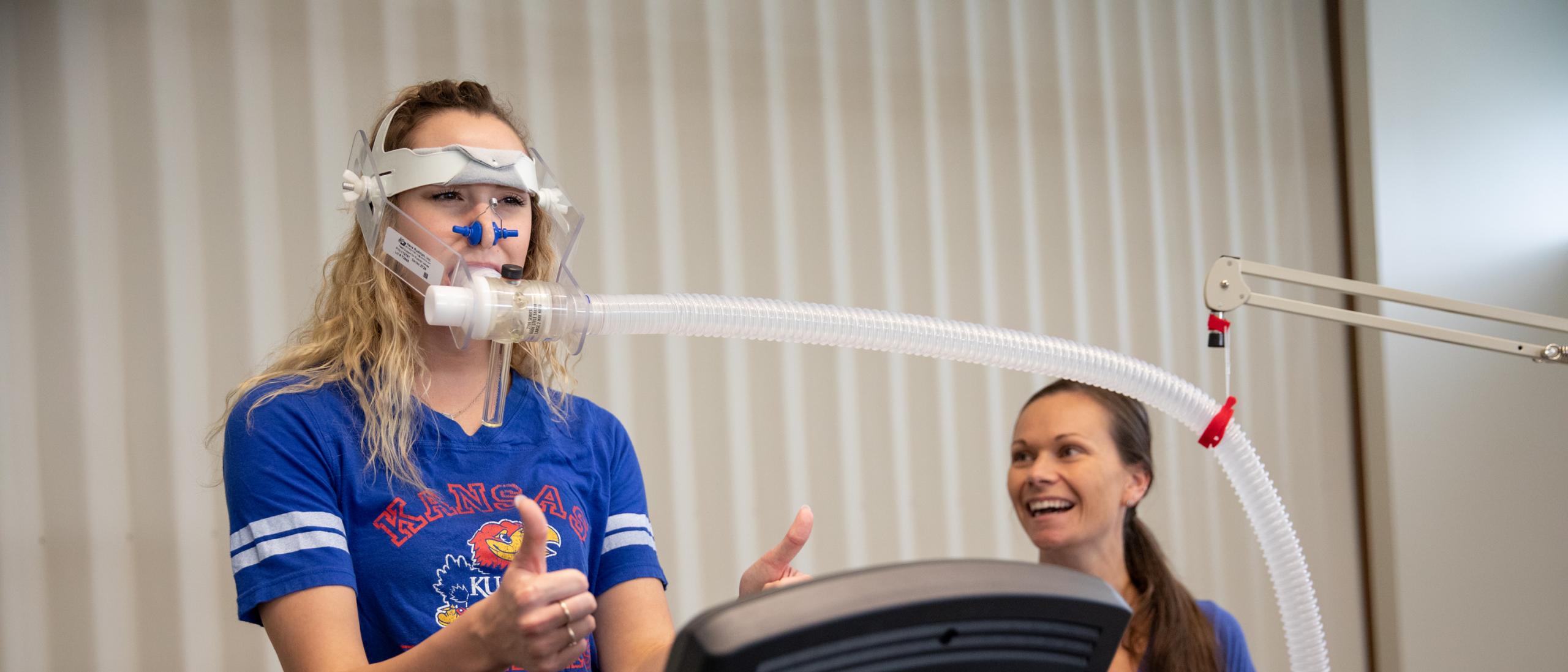 Student on treadmill with breathing apparatus giving thumbs up with Dr. Ashley Herda on the right side 